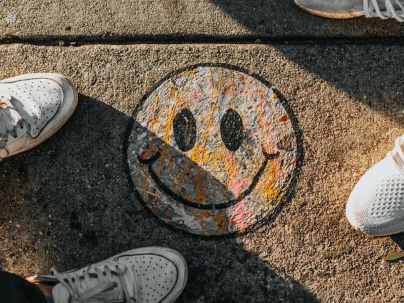 Colorful smiley face with paint drips painted on a sidewalk, surrounded by sneakers