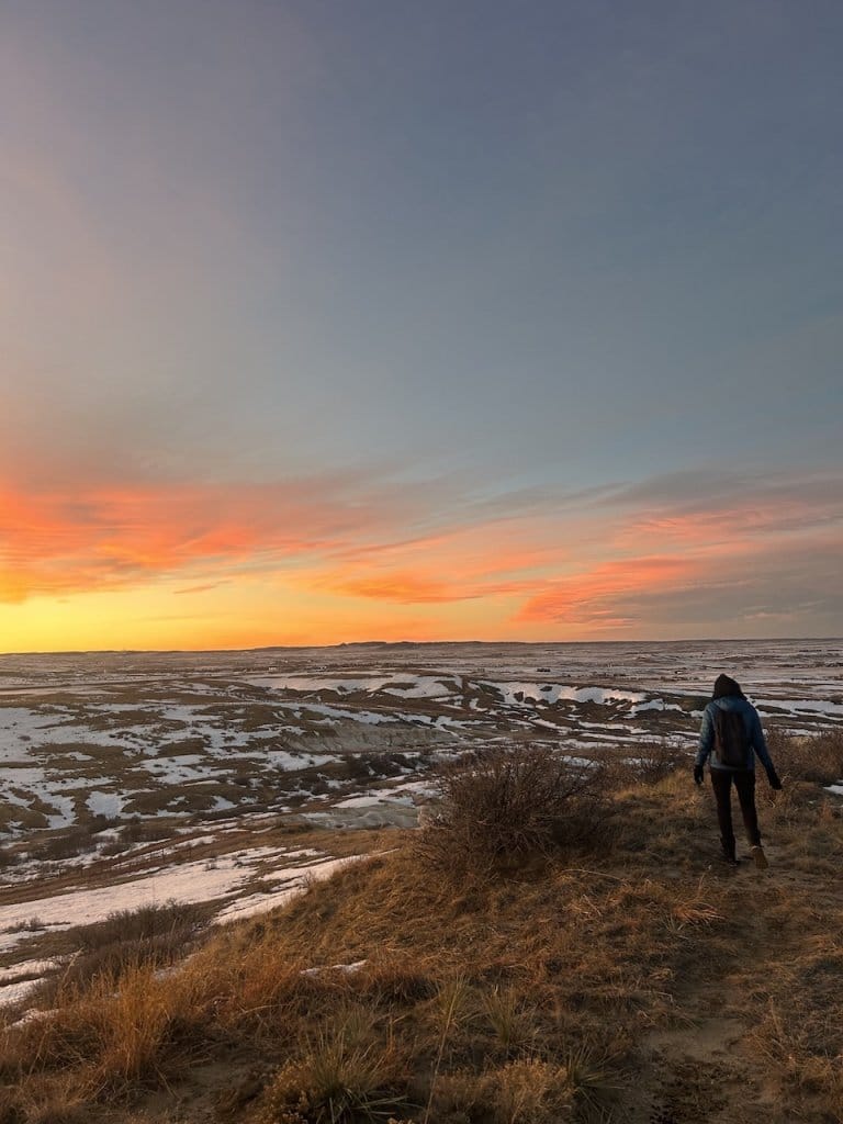 Ben Hoffman standing on a hilltop overlooking a snow-dusted prairie at sunset