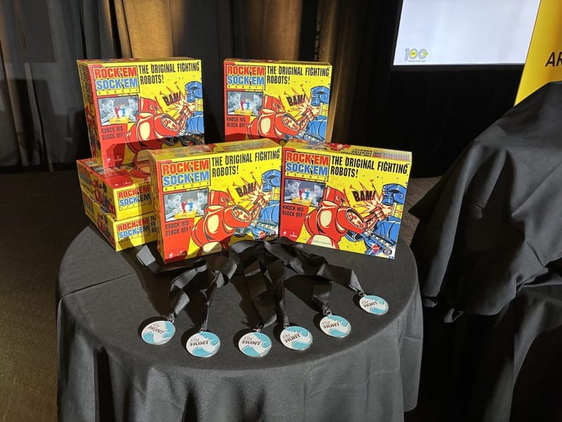 Rock Em Sock Em Robots game boxes and cityHUNT medals displayed on a table as Battle Bots event prizes