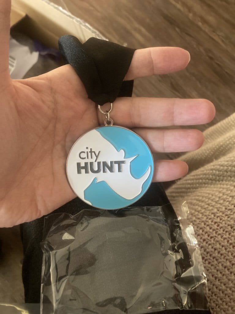 Hand holding a cityHUNT winner medal with black ribbon