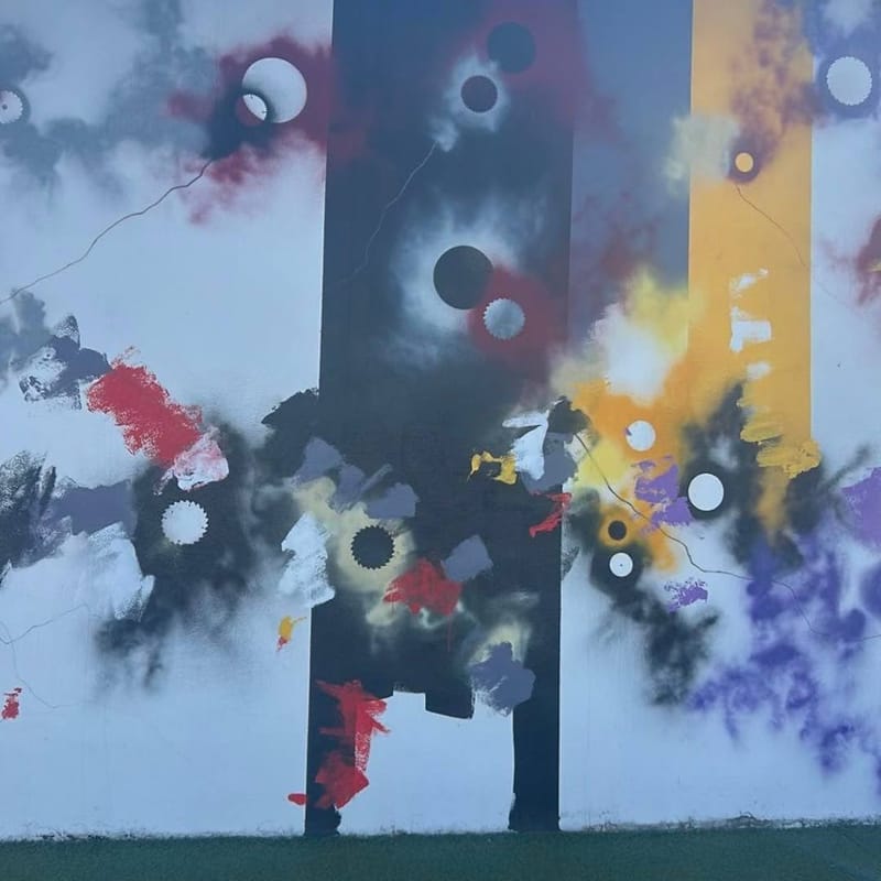 Large abstract outdoor mural with gear shapes and bold paint splashes in red, yellow, purple, and black